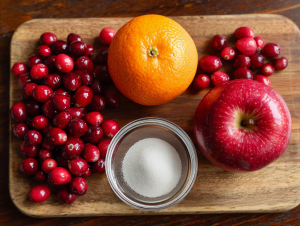 The 5 ingredients for the fresh cranberry relish recipe: cranberries, a whole orange, a sweet apple, sugar, and salt.